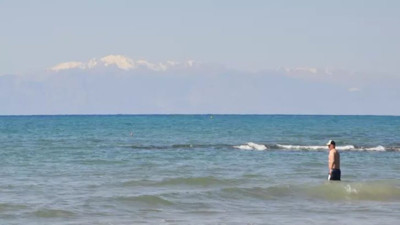 Karlı dağ manzarasında denize girdiler. Sıcak havayı fırsat bilen turistler sahillere akın etti