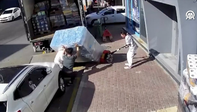 Devrilen yüzlerce kilo su yüklü paletin altında kaldılar. O anlar anbean kameraya yansıdı