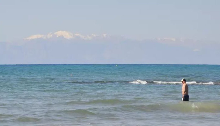 Karlı dağ manzarasında denize girdiler. Sıcak havayı fırsat bilen turistler sahillere akın etti